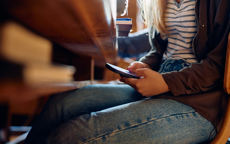 Frau benutzt Smartphone unter einem Tisch versteckt. Foto: Drazen/stock.adobe.com