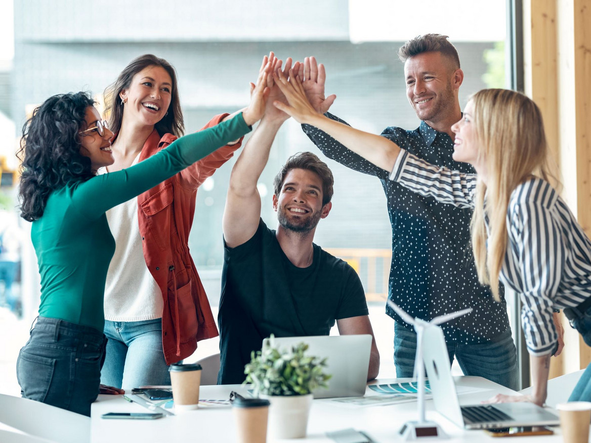 Eine Gruppe junger Berufstätiger am Arbeitstisch mit Laptop beim Feiern eines Erfolgs. Foto: nenetus - stock.adobe.com