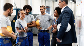 Diverses Produktionsteam mit Helmen und Arbeitshosen bei einer Besprechung. Foto: Drazen - stock.adobe.com