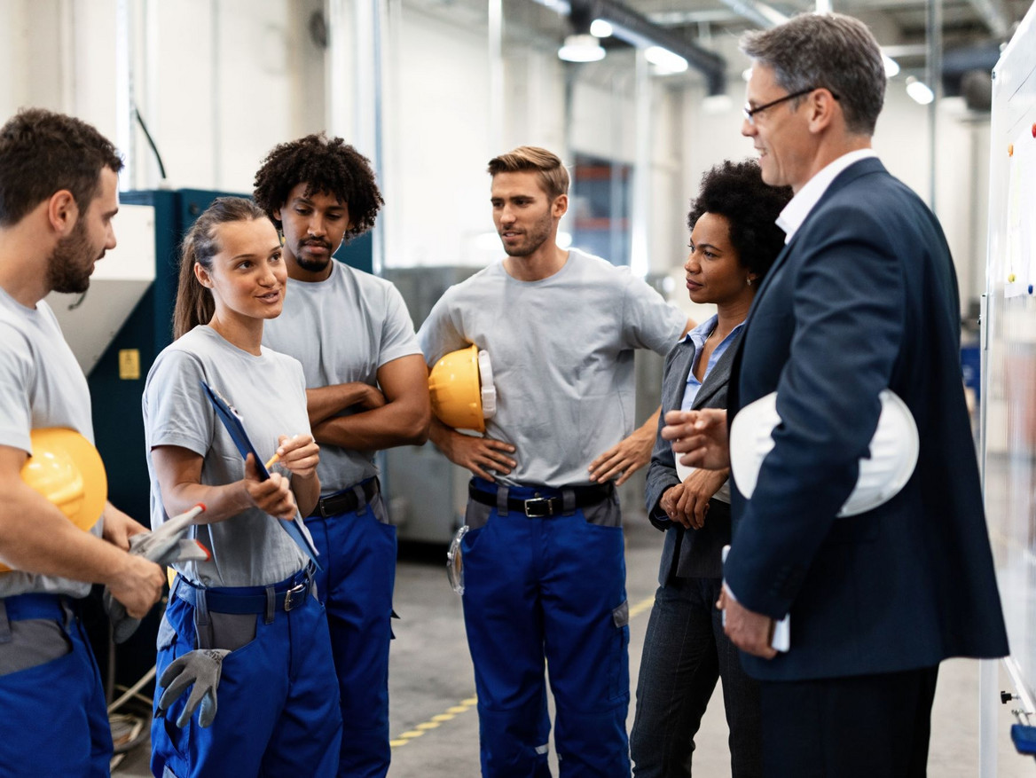 Diverses Produktionsteam mit Helmen und Arbeitshosen bei einer Besprechung. Foto: Drazen - stock.adobe.com