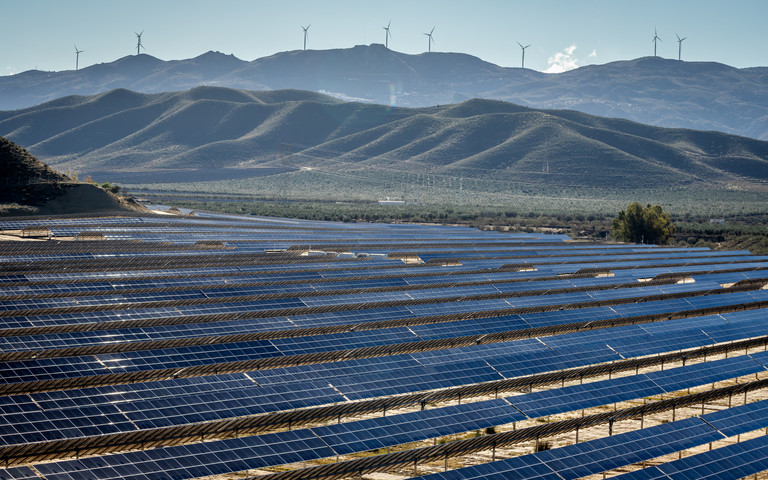 Ein Solarpark in Andalusien ist im Vordergrund zu sehen, dahinter Berge und Windräder. (Foto: stock.adobe.com – Alice_D)