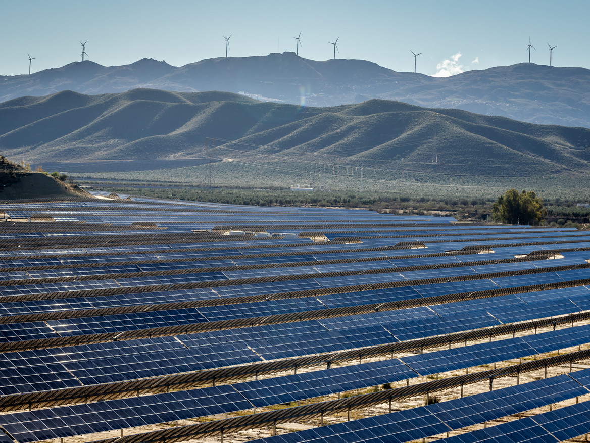 Ein Solarpark in Andalusien ist im Vordergrund zu sehen, dahinter Berge und Windräder. (Foto: stock.adobe.com – Alice_D)