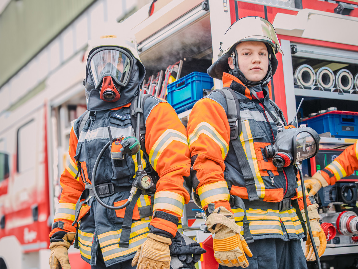 Zwei Männer in Feuerwehruniform stehen vor einem Feuerwehrauto. Foto: IW Medien / Joshua Murat