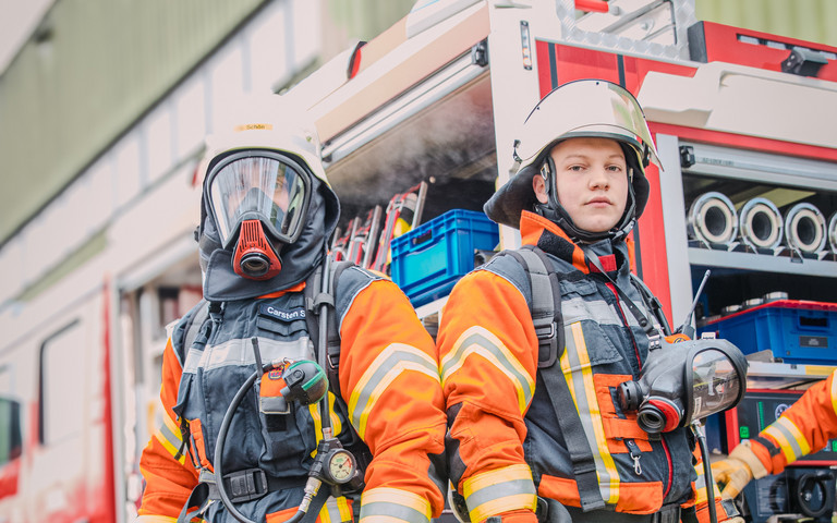 Zwei Männer in Feuerwehruniform stehen vor einem Feuerwehrauto. Foto: IW Medien / Joshua Murat