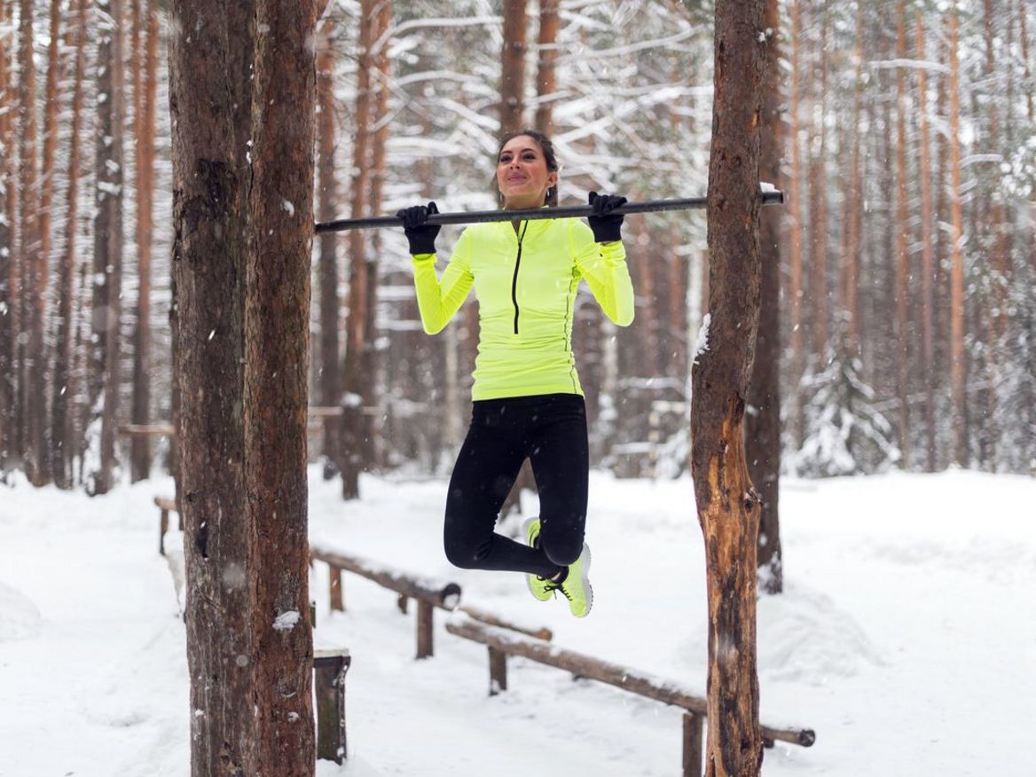 Eine Frau macht Fitnessübungen an einer Anlage im Wald.