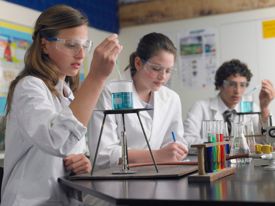 Drei Schüler sitzen mit weißen Kitteln in einem Chemieraum und experimentieren. Foto: stock.adobe.com/moodboard