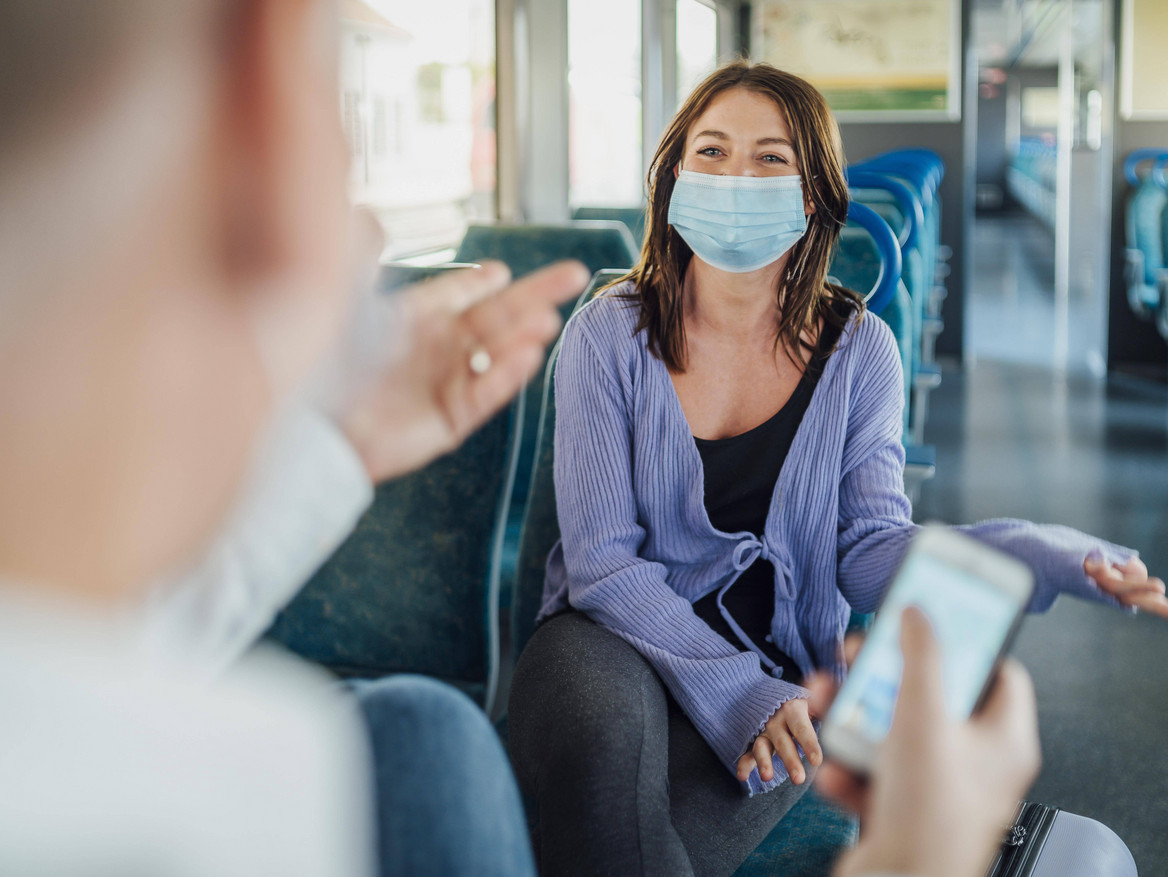 Zwei Reisende mit Maske unterhalten sich in einem Zug.