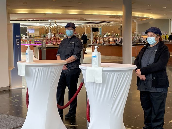 Zwei Mitarbeiter mit medizinischen Masken stehen in einer Kantine