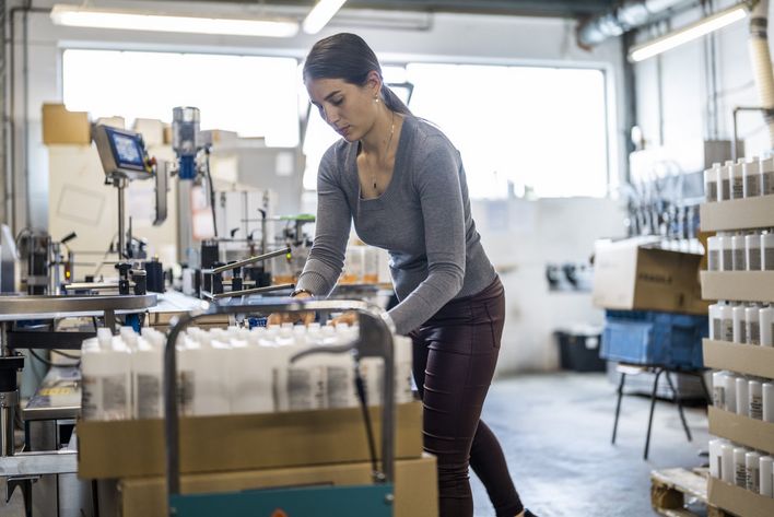 Eine Frau verpackt Flaschen mit Reinigungsmitteln in einer Fabrikhalle