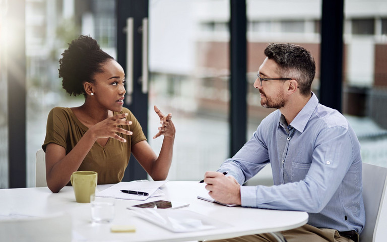 Zwei Berufstätige in einem konstruktiven Dialog am Arbeitstisch. Foto: Katleho Seisa peopleimages.com - stock.adobe.com